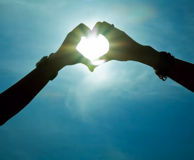 Corazón formado con la manos con el sol de fondo